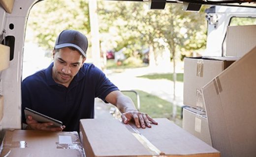 Courier With Digital Tablet Checking Packages In Van