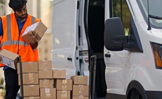 A medium wide shot of a young, delivery person examining boxes in front of his van.