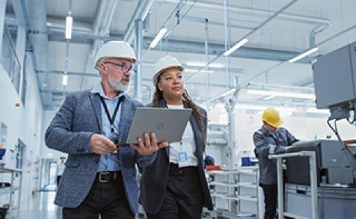 Two Professional Heavy Industry Engineers Wearing Hard Hats at Factory. Walking and Discussing Industrial Machine Facility, Working on Laptop. African American Manager and Technician at Work.