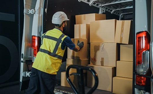Handsome Latin Male Worker Wearing Hard Hat Loads Cardboard Boxes into Delivery Truck. Delivering Online Orders, E-Commerce Goods, Food, Medicine Supply. Overworked Tired Frontline Hero Doing Job